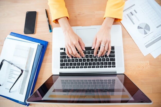 A close-up of hands typing on a laptop, surrounded by documents such as loan statements and credit reports.