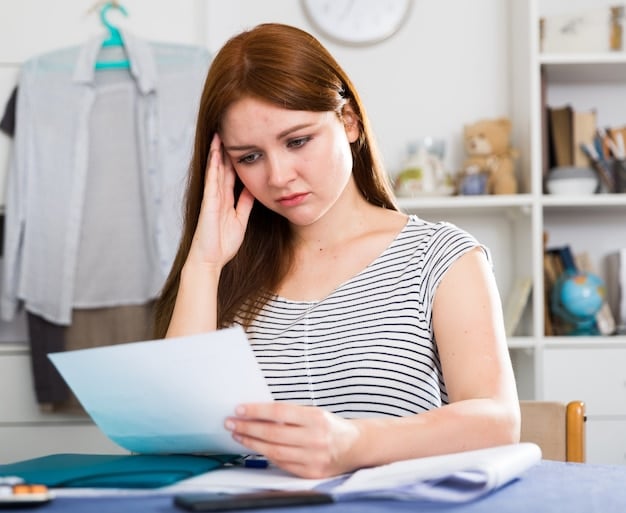 A concerned-looking student holding their head in their hands while looking at a laptop displaying a student loan debt statement.